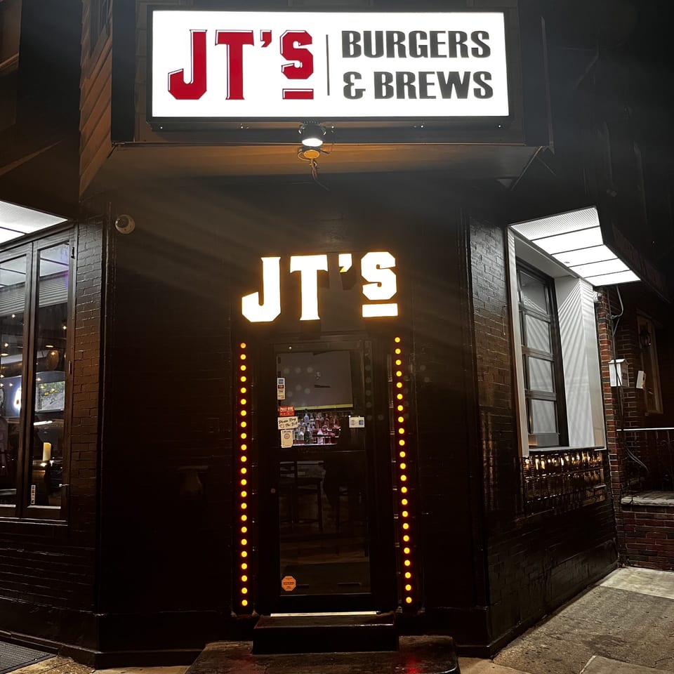 Exterior of JT's Burgers & Brews at night, with illuminated signs and entrance lights.
