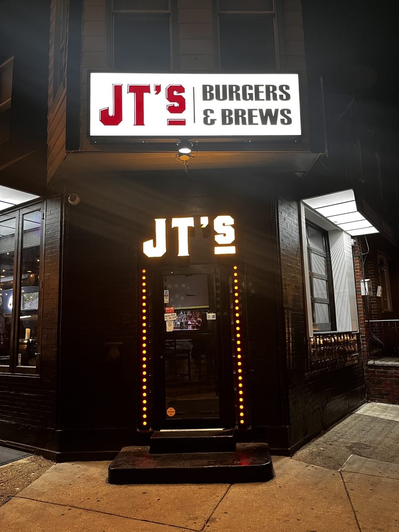 Exterior of JT's Burgers & Brews at night, with illuminated signs and entrance lights.
