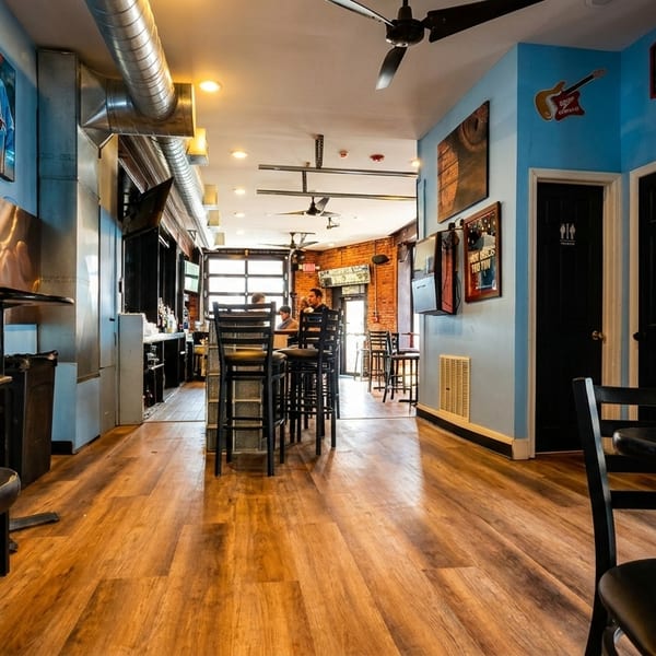 Interior of a restaurant with light blue walls, wooden floors, black tables, and a bar area.